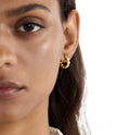 Close-up of a woman wearing gold hoop earrings with a neutral background