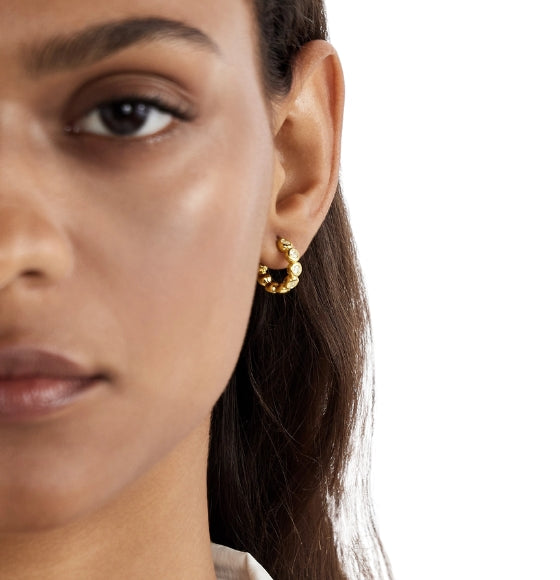 Close-up of a woman wearing gold hoop earrings with a neutral background