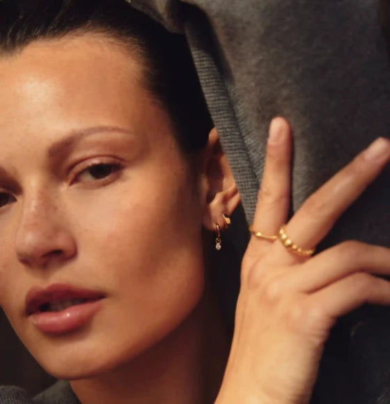 Close-up of a woman's face with a hand touching her cheek, wearing gold jewelry.