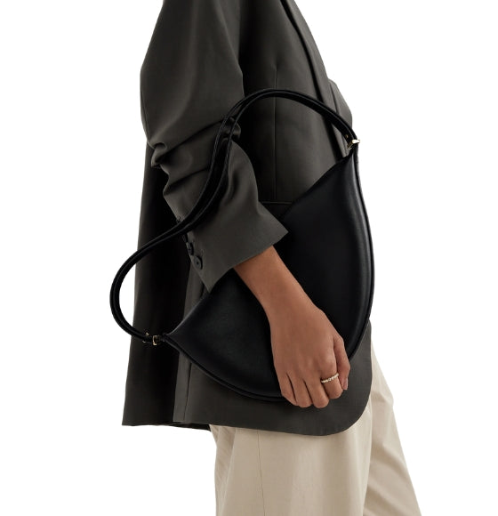 Person holding a black handbag with a plain background and gemstone ring